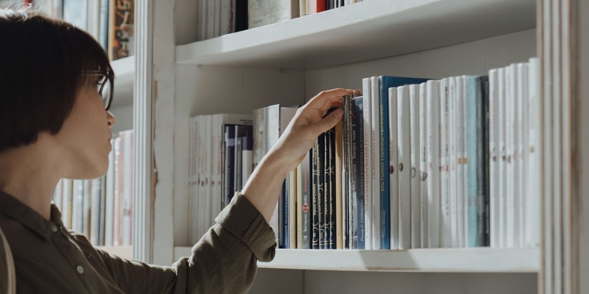 A reader explores various titles on a bookshelf, searching for their next dark fantasy adventure.